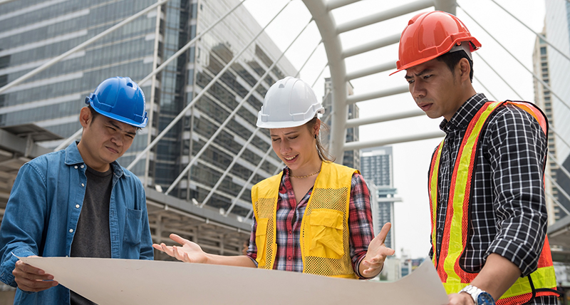 Three construction workers on a site looking at a large paper drawing